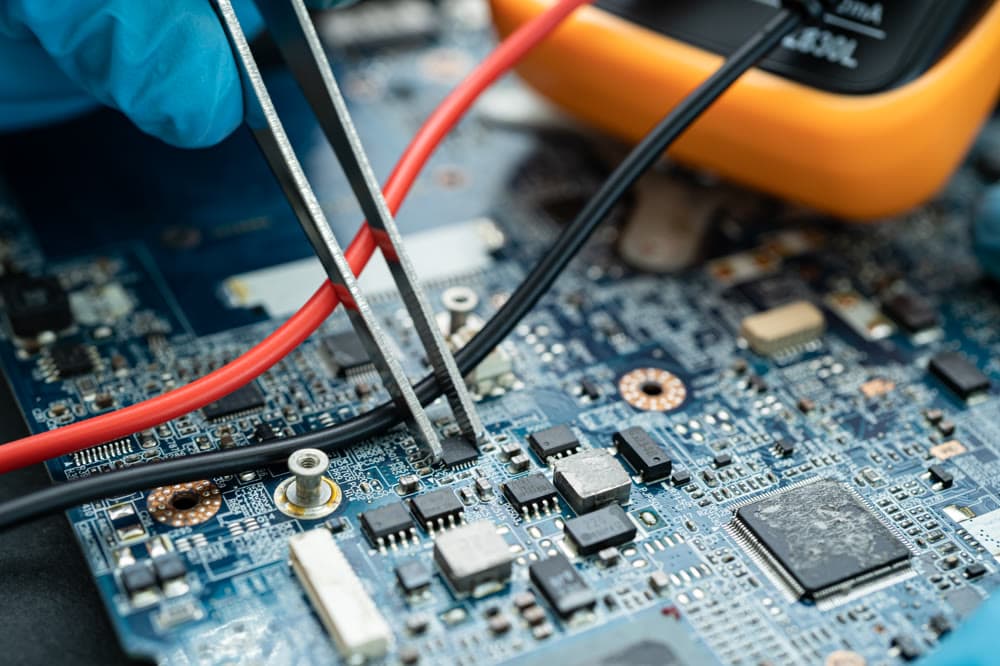 Mains gantées sondant une carte au multimètre et à la pince, diagnostic d'un instrument en panne
