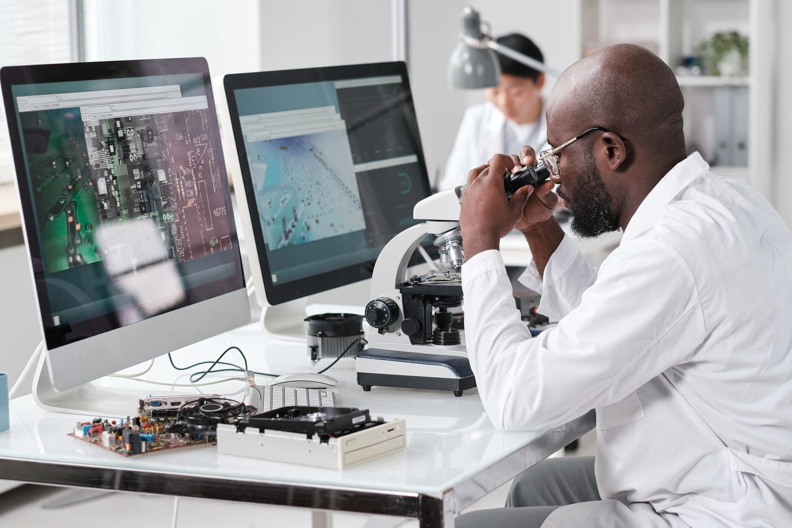 Technicien en blouse analysant une carte électronique au microscope, relevés de diagnostic affichés à l'écran